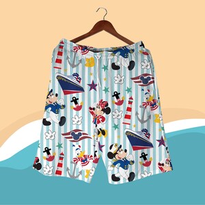 May include: Light blue and white striped shorts featuring a nautical theme with cartoon characters. The shorts have an elastic waistband and are decorated with images of Mickey Mouse, Minnie Mouse, Donald Duck, ships, anchors, and lighthouses.