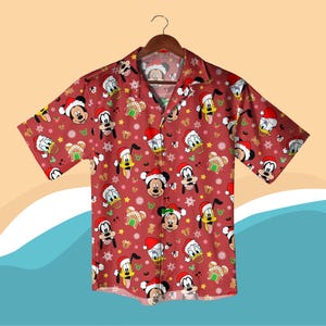 Puede incluir: Camisa roja de manga corta con un estampado navideño con personajes de Disney como Mickey Mouse y Donald Duck con gorros de Papá Noel. El diseño también incluye casas de jengibre y copos de nieve. La camisa tiene un cuello clásico.
