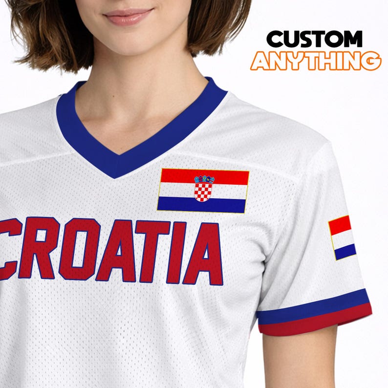 K&ouml;nnte beinhalten: Wei&szlig;es Trikot mit blauem V-Ausschnitt und rot-blauen &Auml;rmelbesatz. Das Wort "CROATIA" ist rot &uuml;ber die Brust gedruckt. Eine kroatische Flagge ist auf Brust und &Auml;rmel abgebildet. Der Text "CUSTOM ANYTHING" befindet sich oben rechts.
