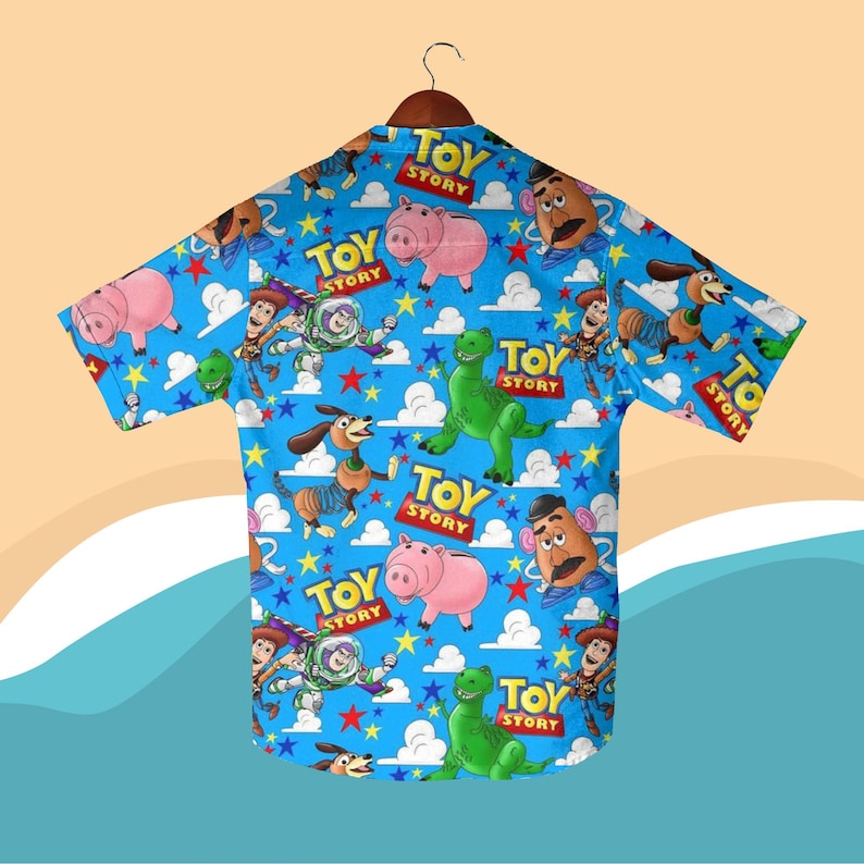 K&ouml;nnte beinhalten: Ein kurz&auml;rmeliges Hemd mit einem farbenfrohen Muster von Figuren aus dem Animationsfilm "Toy Story". Das Design zeigt Woody, Buzz Lightyear, Rex, Hamm und Mr. Potato Head auf blauem Hintergrund mit Wolken, Sternen und den Worten "Toy Story".
