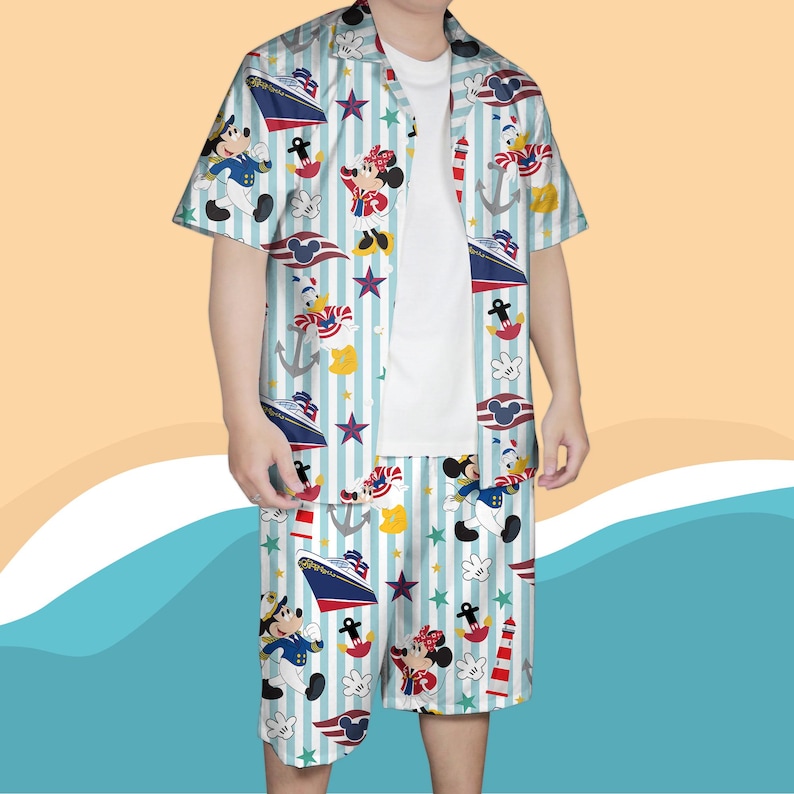 May include: A two-piece matching set featuring a short-sleeved button-down shirt and shorts. The set is light blue with vertical white stripes and a nautical-themed print of cartoon characters, ships, anchors, and stars. The shirt is open, revealing a white t-shirt underneath.