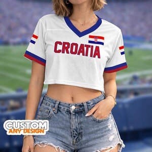 K&ouml;nnte beinhalten: Wei&szlig;es Crop-Top mit V-Ausschnitt und dem Wort "CROATIA" in Rot. Das Oberteil hat die kroatische Flagge und blaue und rote Akzente. Die &Auml;rmel haben blaue und rote Streifen. Der Text "CUSTOM ANY DESIGN" befindet sich unten.