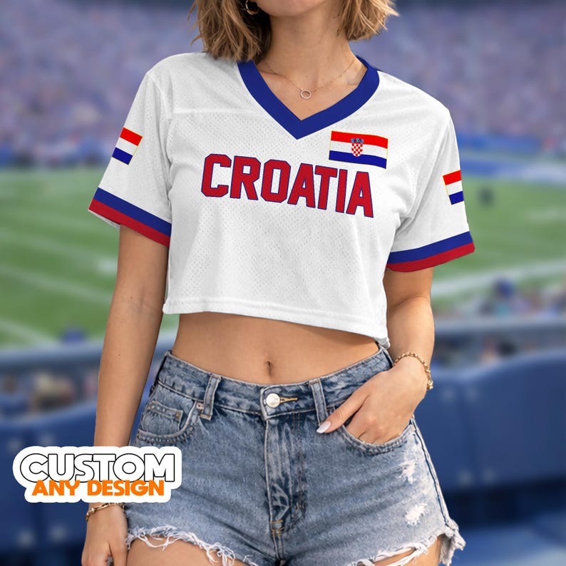 K&ouml;nnte beinhalten: Wei&szlig;es Crop-Top mit V-Ausschnitt und dem Wort "CROATIA" in Rot. Das Oberteil hat die kroatische Flagge und blaue und rote Akzente. Die &Auml;rmel haben blaue und rote Streifen. Der Text "CUSTOM ANY DESIGN" befindet sich unten.