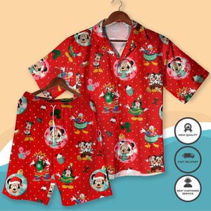 Puede incluir: Un conjunto de camisa y pantalón corto rojos con temática navideña. El conjunto presenta un patrón repetido de Mickey Mouse, Minnie Mouse y Donald Duck con atuendos festivos. La camisa tiene mangas cortas y cuello clásico. El pantalón corto tiene cintura con cordón.