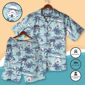 Pode incluir: Um conjunto de camisa havaiana e calções Star Wars azul claro. O conjunto apresenta um padrão repetido de capacetes Stormtrooper, andadores AT-AT e palmeiras. A camisa tem mangas curtas e uma frente abotoada. Os calções têm cintura com cordão.