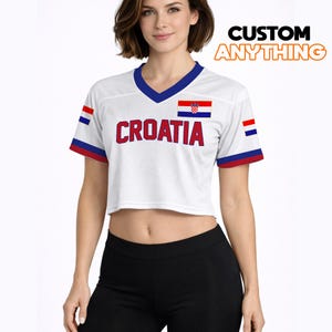 K&ouml;nnte beinhalten: Wei&szlig;es Crop-Top mit blauem V-Ausschnitt und roten und blauen Akzenten. Das Shirt tr&auml;gt das Wort "CROATIA" in roten Blockbuchstaben und die kroatische Flagge. Der Text "CUSTOM ANYTHING" ist orange.