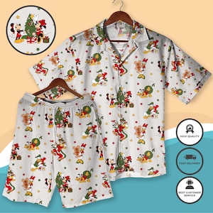 Puede incluir: Un conjunto de pijama blanco con temática navideña que presenta una camisa con botones de manga corta y pantalones cortos a juego. El conjunto está adornado con personajes de dibujos animados festivos, árboles de Navidad y cajas de regalo.