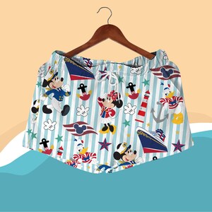 May include: Light blue and white striped shorts featuring cartoon characters Mickey Mouse, Minnie Mouse, and Donald Duck in nautical attire. The shorts have a drawstring waist and are decorated with anchors, stars, and a cruise ship.