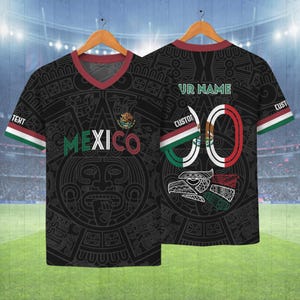 May include: Black soccer jersey with a V-neck and short sleeves. The jersey features the word "MEXICO" in green and red, a Mexican coat of arms, and a large Aztec-inspired design. The back has the number "0" and space for a name.