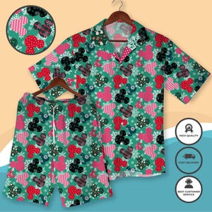 Può includere: Un completo composto da camicia e pantaloncini verdi con un motivo di cuori rossi e rosa, sagome nere di Topolino e fiocchi di neve bianchi. La camicia a maniche corte e i pantaloncini hanno la vita con coulisse. Il completo è esposto su una gruccia di legno.