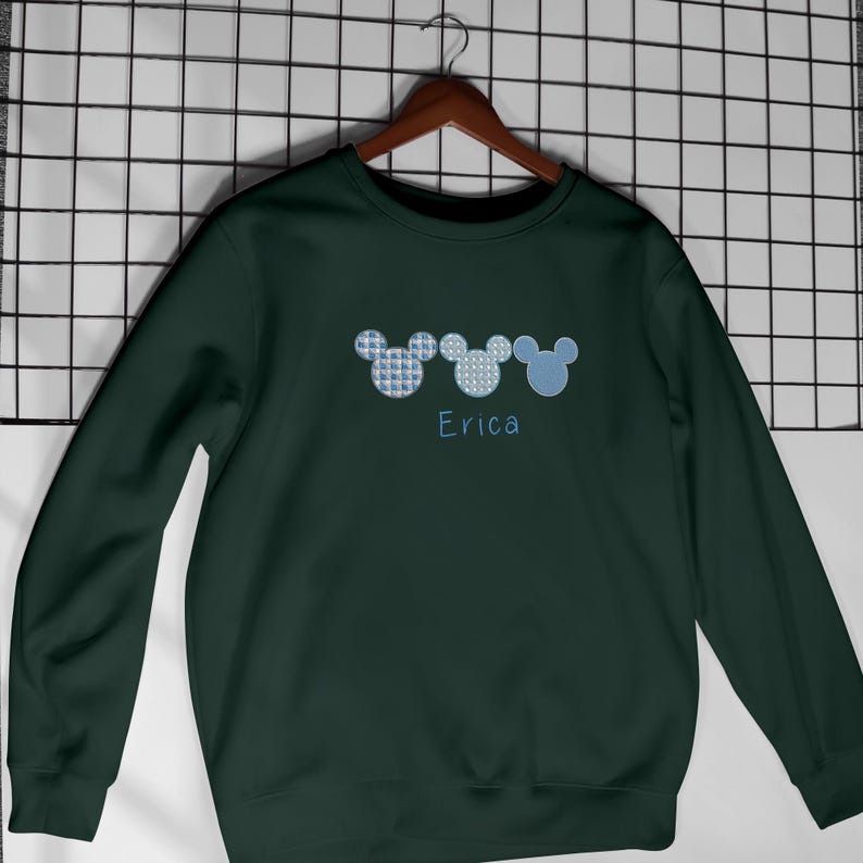 May include: A dark green sweatshirt with three blue Mickey Mouse heads embroidered on the front. The name "Erica" is embroidered below the heads.