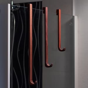 May include: Three wooden hooks hang from a glass shower door. The hooks are a reddish-brown colour and have a simple, curved design.