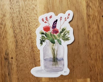Può includere: Adesivo ad acquerello con una composizione floreale in un barattolo di vetro. Il bouquet comprende bacche rosse, fiori viola e fogliame verde. Il barattolo ha una linea d'acqua e un bordo bianco. L'adesivo è su una superficie di legno.