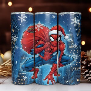 Puede incluir: Tres vasos de acero inoxidable con un diseño invernal. La imagen muestra a Spider-Man con un gorro de Papá Noel, llevando un saco rojo, sobre un paisaje urbano nevado. Los vasos son cilíndricos y tienen un acabado brillante.