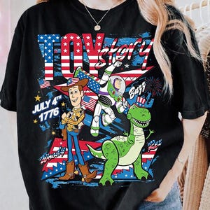 May include: Black t-shirt featuring a graphic of characters from Toy Story, including Woody, Buzz Lightyear, and Rex, with an American flag design. The text "Toy Story" and "July 4th 1776" are also visible.