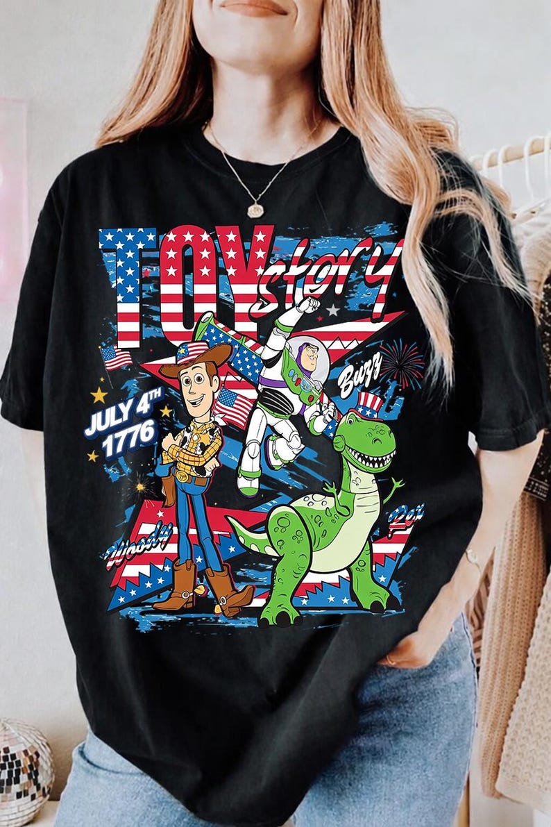 May include: Black t-shirt featuring a graphic of characters from Toy Story, including Woody, Buzz Lightyear, and Rex, with an American flag design. The text "Toy Story" and "July 4th 1776" are also visible.