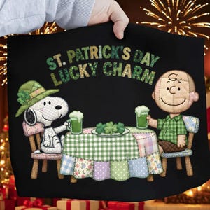 Puede incluir: Gráfico negro con temática del Día de San Patricio con Snoopy y Charlie Brown brindando con cerveza verde. La mesa tiene un mantel de retazos con tréboles. El texto dice "St. Patrick's Day Lucky Charm".
