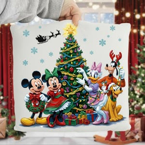 Puede incluir: Un cojín cuadrado blanco con una escena navideña con Mickey Mouse, Minnie Mouse, Daisy Duck, Goofy y Pluto. Un árbol de Navidad decorado está en el centro, con copos de nieve y el trineo de Papá Noel en el fondo. Los personajes visten atuendos festivos.