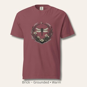 Flat lay of a Comfort Colors 1717 t-shirt in Brick, showcasing the Dragonfly Sigil with wildflowers and crescent moon. Warm, grounded, vintage-washed cotton. Perfect for dark feminine, witchy, and nature-inspired wardrobes.