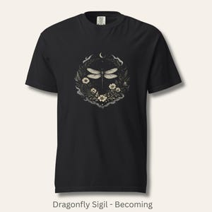 Flat lay of Comfort Colors 1717 t-shirt in soft vintage blue, featuring a detailed dragonfly sigil surrounded by botanical linework and a crescent moon. Witchy, nature-inspired, dark feminine aesthetic. Garment-dyed cotton with a relaxed fit. Ideal for intuitive women, symbolic style, and emotional healing wardrobes.