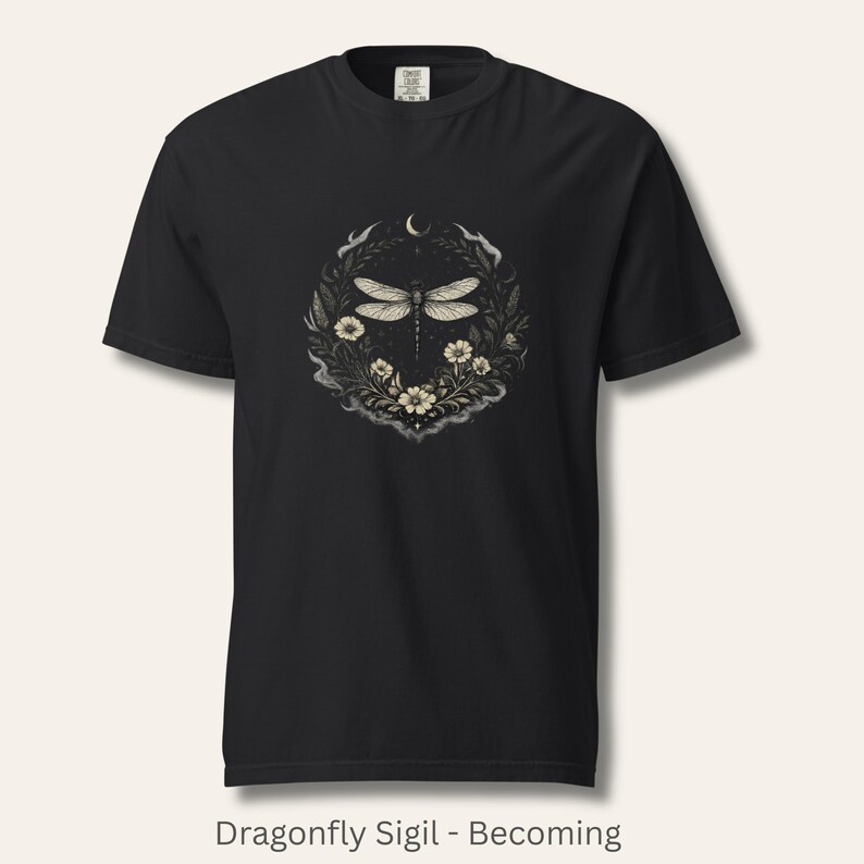 Flat lay of Comfort Colors 1717 t-shirt in soft vintage blue, featuring a detailed dragonfly sigil surrounded by botanical linework and a crescent moon. Witchy, nature-inspired, dark feminine aesthetic. Garment-dyed cotton with a relaxed fit. Ideal for intuitive women, symbolic style, and emotional healing wardrobes.