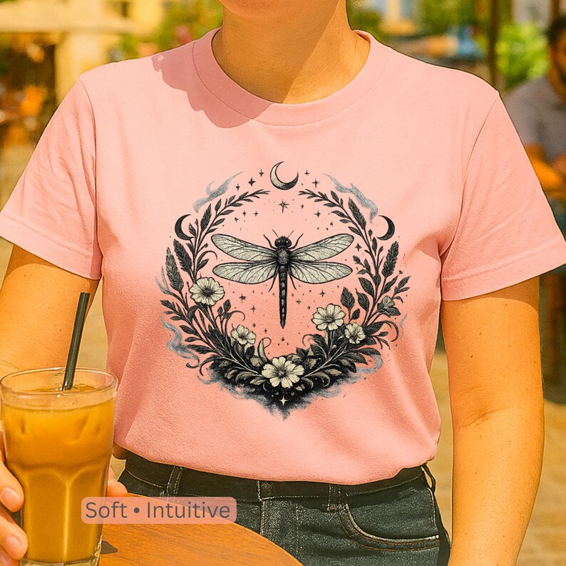 Model wearing Comfort Colors 1717 t-shirt in Blossom, seated in a cozy indoor space with soft lighting. Dragonfly Sigil visible on front. Feminine, symbolic, emotionally resonant design. Ideal for journaling, rituals, and healing seasons.