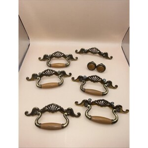 May include: A set of antique brass cabinet hardware, including handles and knobs. The handles have a decorative, ornate design with a wooden grip. The knobs are round with a matching finish.