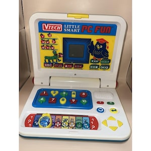 May include: A white and blue VTech Little Smart PC Fun laptop toy. The toy features a screen, number and letter buttons, and a keyboard. The laptop has a yellow top and a blue base. The screen displays an owl wearing a graduation cap.