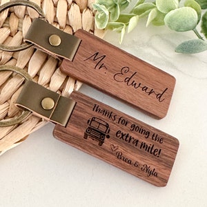 May include: Two wooden keychains with leather straps and key rings. One keychain has the text "Mr. Edward" engraved on it. The other keychain has the text "Thanks for going the extra mile! Brea & Nyla" engraved on it, along with a small image of a school bus.