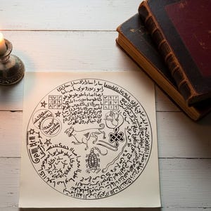 Könnte beinhalten: Eine handgezeichnete, kreisförmige Illustration mit komplizierten Schriftzügen und Symbolen, die Tierfiguren und geometrische Formen zeigt. Das Kunstwerk befindet sich auf cremefarbenem Papier, mit zwei antiken Büchern und einem Kerzenhalter im Hintergrund.