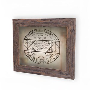May include: A framed print with a brown wooden frame. The print features a circular design with Arabic text and symbols. The text reads "Ya Razzaq" which translates to "O Provider".
