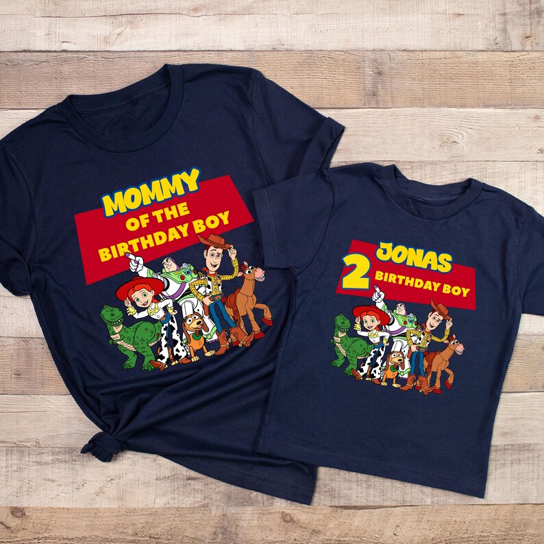 May include: Two navy blue t-shirts with a Toy Story theme. The larger shirt says "Mommy of the Birthday Boy" and features the characters Woody, Buzz Lightyear, Jessie, Rex, Slinky Dog, and Bullseye. The smaller shirt says "2 Jonas Birthday Boy" and features the same characters.