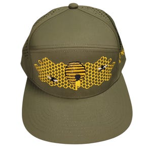 Op de afbeelding: Olijfgroene baseballpet met een honingraat- en bijenontwerp. De pet heeft een gebogen klep en een geperforeerde bovenkant. Het geborduurde ontwerp omvat een gele honingraat, een bijenkorf en twee bijen.