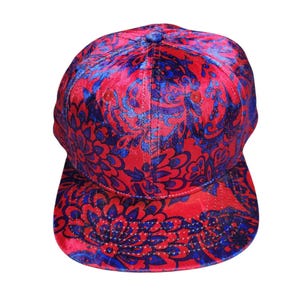 May include: A red and blue patterned baseball cap. The cap features a floral design in shades of red and blue. The cap has a curved brim and a rounded crown.