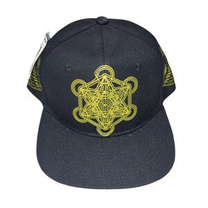 May include: A black baseball cap featuring a yellow geometric design on the front. The design is a complex pattern of overlapping circles and lines.