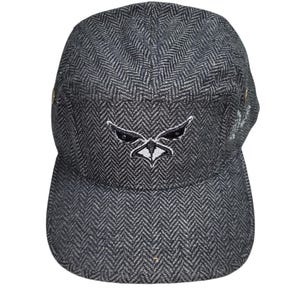 May include: A dark gray and black herringbone patterned five-panel cap featuring a centered embroidered graphic of a stylized bird head in black and white thread. The cap has a flat brim and small metallic side eyelets for ventilation.
