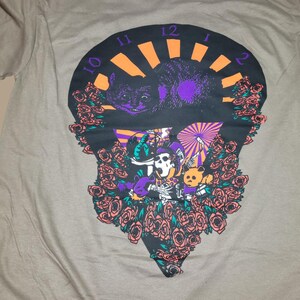 May include: A gray t-shirt with a black and purple graphic print of a clock face with a cat, a skeleton, and a bear surrounded by roses. The clock face has the numbers 10, 11, 12, 1, and 2.