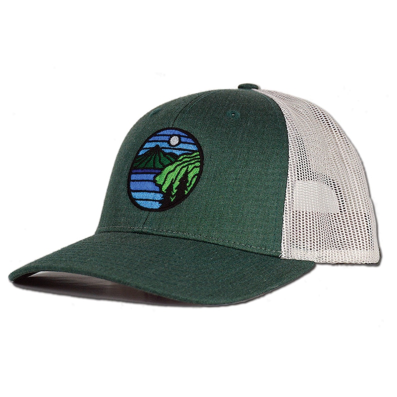 May include: A green and white trucker hat with a circular embroidered patch depicting a mountain scene with a lake and trees. The patch has blue, green, and white colors.