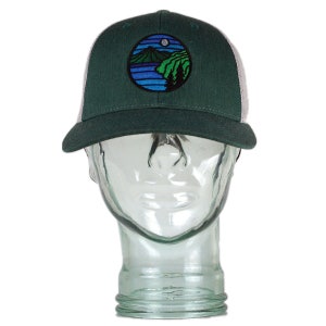 May include: A green and white trucker hat with a circular embroidered patch featuring a mountain scene with a lake and a moon.