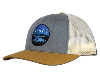 May include: A gray and brown trucker hat with a blue and white embroidered logo that says "TAHOE" with a mountain scene.
