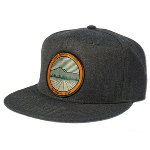 May include: A black and gray fitted baseball cap with a circular patch featuring a mountain range, trees, and the text "Rise Designs - Est. 2007 Mt. Tallac - 9738".