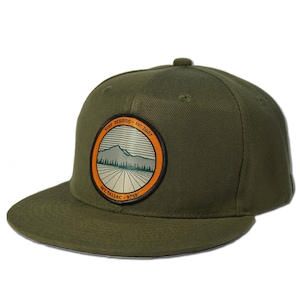 Puede incluir: Una gorra de béisbol verde con un parche circular que presenta una cordillera, árboles y el texto "Rise Designs - Est. 2007" y "Mt. Tallac - 9733'"