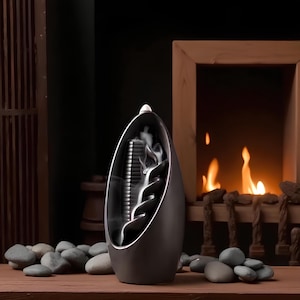 May include: A dark gray incense burner with a spiral design, emitting white smoke. The burner has a sleek, modern aesthetic, and is placed on a wooden surface with gray stones. The background features a fireplace with flames.
