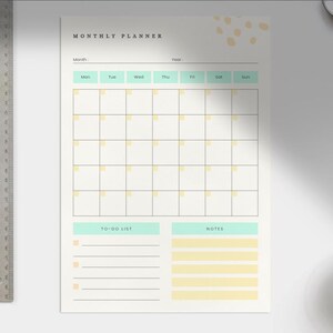 Könnte beinhalten: Ein Monatsplaner mit Rasterlayout zur Planung, mit Abschnitten für To-Do-Listen und Notizen. Der Planer hat einen cremefarbenen Hintergrund mit Minz- und gelben Akzenten. Auf der linken Seite des Bildes befindet sich ein Metalllineal.