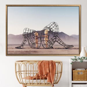 May include: A black metal sculpture of two figures standing in a desert landscape. The figures are made of wire mesh and appear to be embracing.