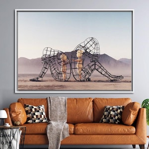 May include: A black metal sculpture of two figures, one larger than the other, standing in a desert landscape. The figures are made of wire mesh and appear to be embracing.