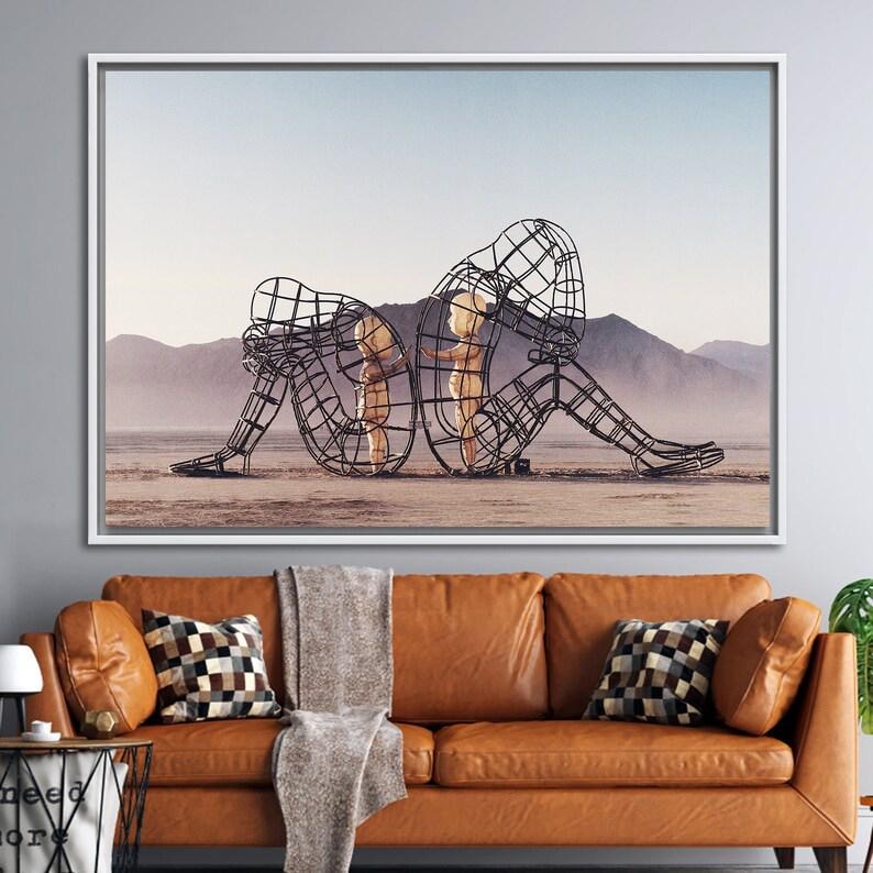 May include: A black metal sculpture of two figures, one larger than the other, standing in a desert landscape. The figures are made of wire mesh and appear to be embracing.