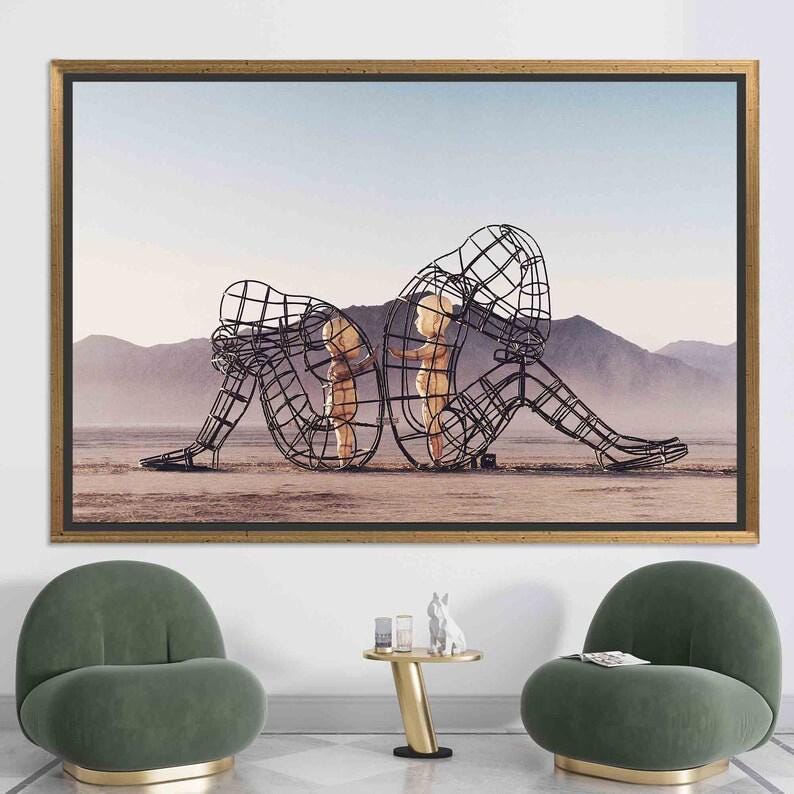 May include: A black and white photograph of three wire frame sculptures in a desert landscape. The sculptures are of two children and an adult, all standing in a line. The adult sculpture is sitting down with their head resting on their hand. The children are standing next to each other, facing the adult.