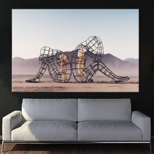 May include: A black and white photograph of a metal sculpture of two figures standing in a desert landscape. The figures are made of wire and appear to be embracing each other.