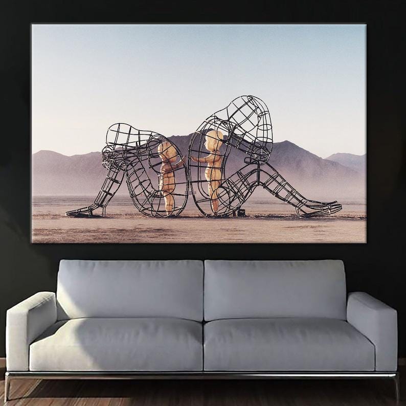 May include: A black and white photograph of a metal sculpture of two figures standing in a desert landscape. The figures are made of wire and appear to be embracing each other.